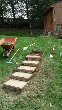 there is a wheelbarrow and shovels on the grass next to some steps