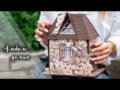 a woman holding a small doll house made out of wood and paper with flowers on it