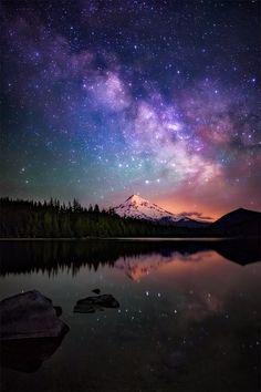 the night sky is filled with stars above a mountain and lake, as well as some rocks