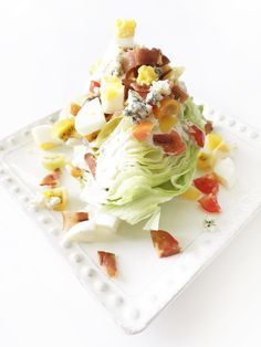 a white plate topped with lettuce covered in bacon and other toppings on top of it