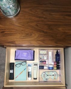 an open drawer with various items in it on top of carpeted floor next to wooden table