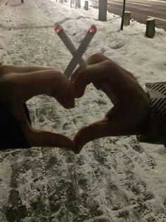 two hands in the shape of a heart on a city street covered in snow with traffic lights