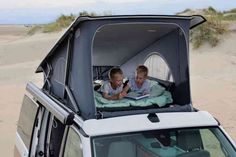 two young boys are sitting in the back of a car with an open tent on top