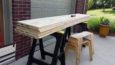 a wooden table sitting on top of a porch next to a garage door and two stools