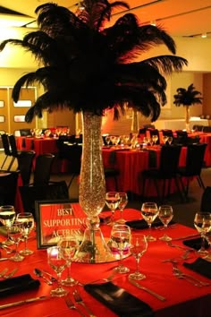 a palm tree in a tall vase on top of a table with wine glasses and place settings