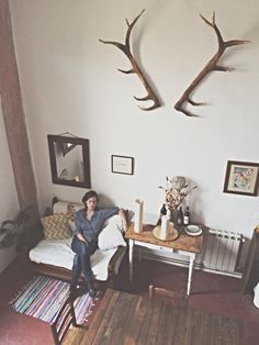 a man sitting on top of a couch in a living room next to antlers