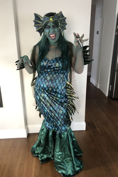 a woman dressed as a mermaid with green hair and blue makeup, holding two hands up in the air