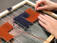 two hands are working on an art project that is being made out of wood and yarn