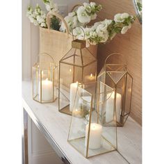 three gold lanterns with white flowers and candles on a table in front of a mirror