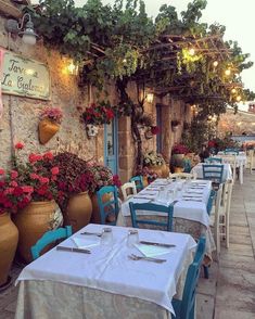 an outdoor dining area with tables, chairs and potted plants on the outside wall