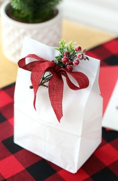 a small white bag with a red bow on it sitting on a table next to a potted plant