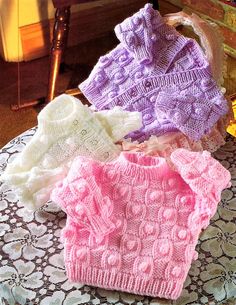 three knitted sweaters sitting on top of a doily next to a fireplace