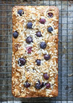 a loaf of bread with blueberries and coconut on top is cooling on a wire rack