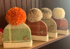 three hats with pom - poms are lined up on a shelf next to an apple