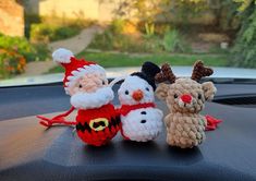 three crocheted christmas ornaments sitting on top of a car's dash board