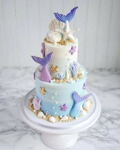 a three tiered cake decorated with mermaids and seashells