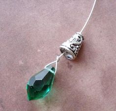 a necklace with a green crystal stone hanging from it's side on a pink surface