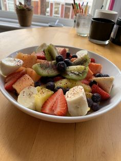 a white bowl filled with sliced fruit on top of a wooden table next to a window