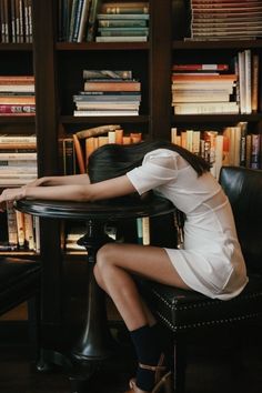 a woman sitting on a chair in front of a book shelf