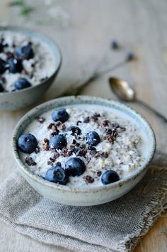 two bowls filled with oatmeal and blueberries on top of a table