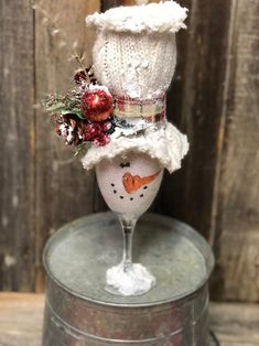 a wine glass with a snowman hat on top and flowers in the bottom, sitting on an old tin can