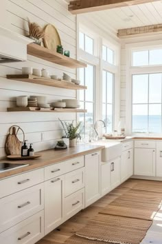 a kitchen with white cabinets and open shelves on the wall, along with an ocean view