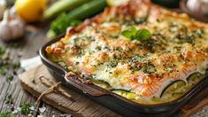 a casserole dish with cheese and vegetables on a wooden table next to lemons