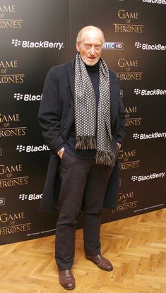 an older man standing in front of a game of thrones sign wearing a scarf