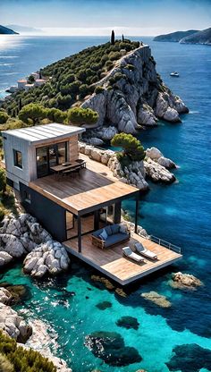 an aerial view of a house in the middle of the ocean with blue water and rocks surrounding it