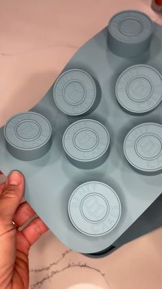 a person holding a tray with nine cupcake pans in front of them on a marble countertop