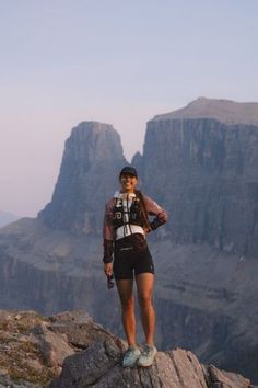 a woman standing on top of a mountain next to a large rocky area with mountains in the background