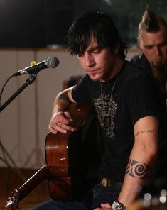 a man sitting in front of a microphone while holding a guitar