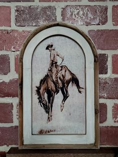 a drawing of a cowboy riding a horse on a brick wall with a wooden frame