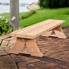 a wooden bench sitting on top of a brick walkway next to a tree and water