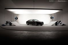 a black car is parked in front of a white backdrop with lights and equipment around it