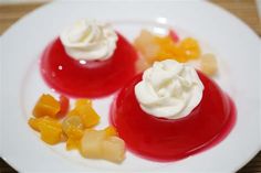 two desserts are on a white plate with fruit toppings and whipped cream in the middle