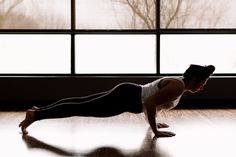 a woman is doing push ups on the floor in front of a window with trees outside