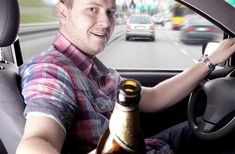 a man sitting in the driver's seat of a car holding a beer bottle