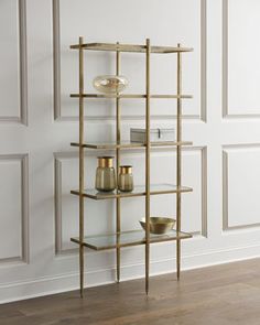 a gold shelf with three vases on it in front of a white painted wall