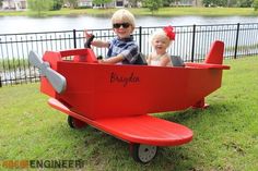 two children are sitting in a red toy plane