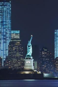 the statue of liberty is lit up at night in new york city, with skyscrapers behind it