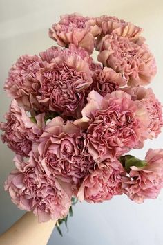 a bunch of pink flowers are in a vase on a white tablecloth with a hand holding it