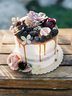 a white cake topped with berries and flowers on top of a wooden table covered in icing