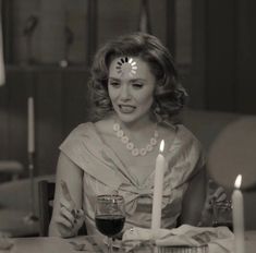 a woman sitting at a table with a candle in front of her and some wine glasses