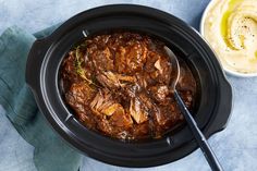 a slow cooker filled with beef stew next to a bowl of mashed potatoes