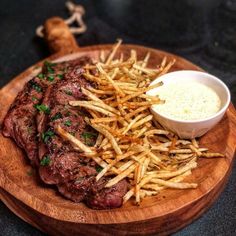 a wooden plate topped with steak and french fries next to a small bowl of ranch dressing