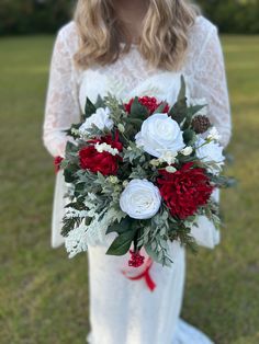 a woman holding a bouquet of red and white flowers on her wedding day in the grass