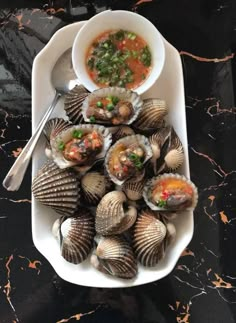 a white plate topped with lots of clams next to a bowl of soup