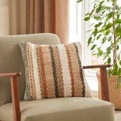 a chair with a pillow on it in front of a potted plant and window