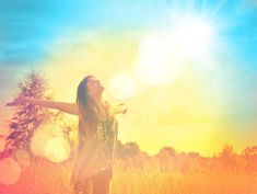 a woman standing in a field with her arms spread out to the sky and trees behind her